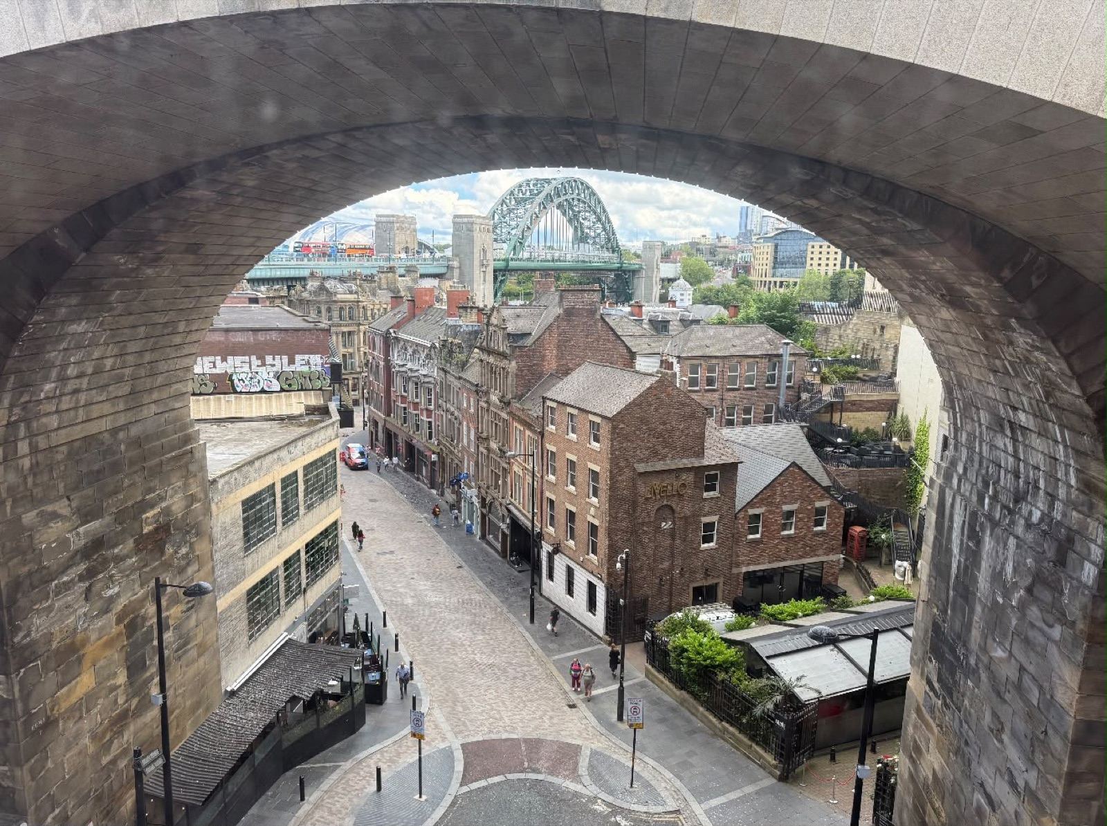 View through a stone railway arch onto Newcastle Quayside, with the Tyne Bridge beyond.